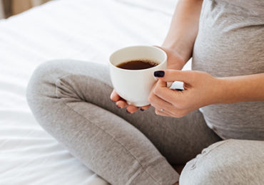 femme-enceinte assise-lit-cafe