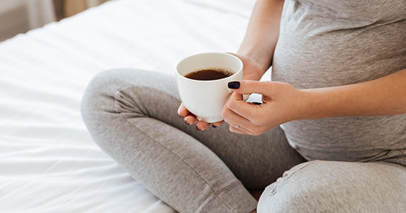 femme-enceinte assise-lit-cafe